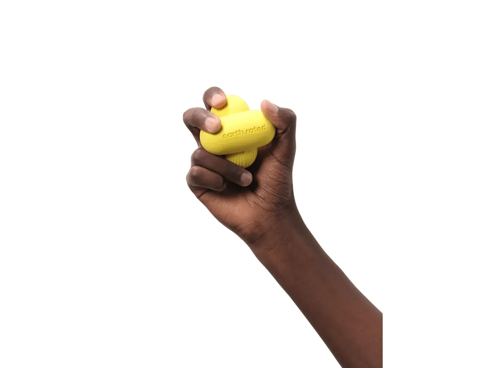 En mørk hånd holder en gul Earth Rated Fetch Toy i naturgummi, med logoen synlig.