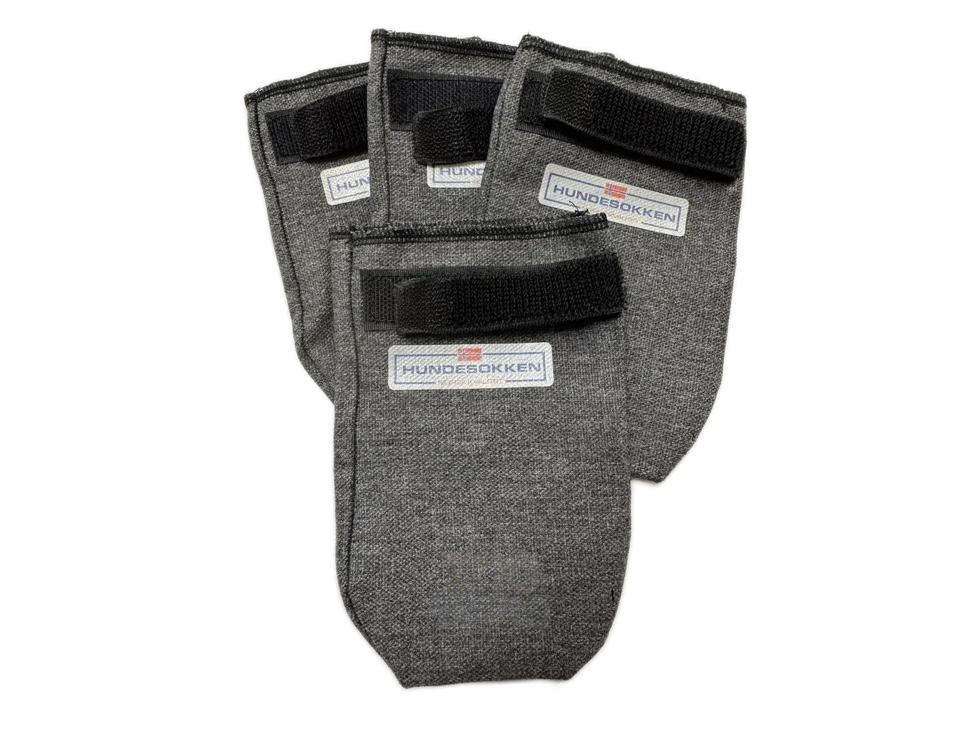 Fire grå denim hundesokker med svart borrelås og etikett med teksten "HUNDESOKKEN - NORSK KVALITET".