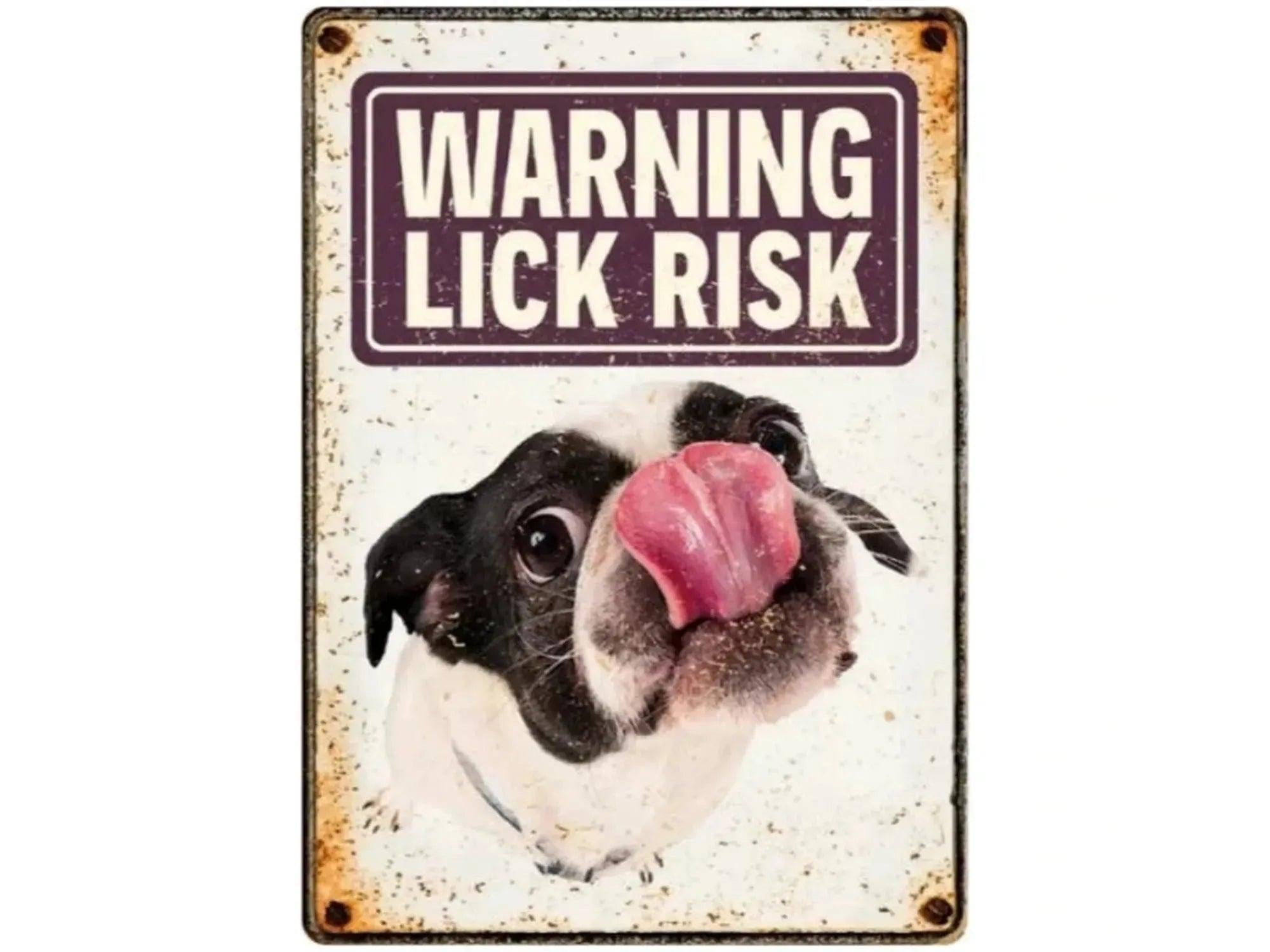Metallskilt med hvit bakgrunn, en svart og hvit hund som slikker, og teksten "WARNING LICK RISK".