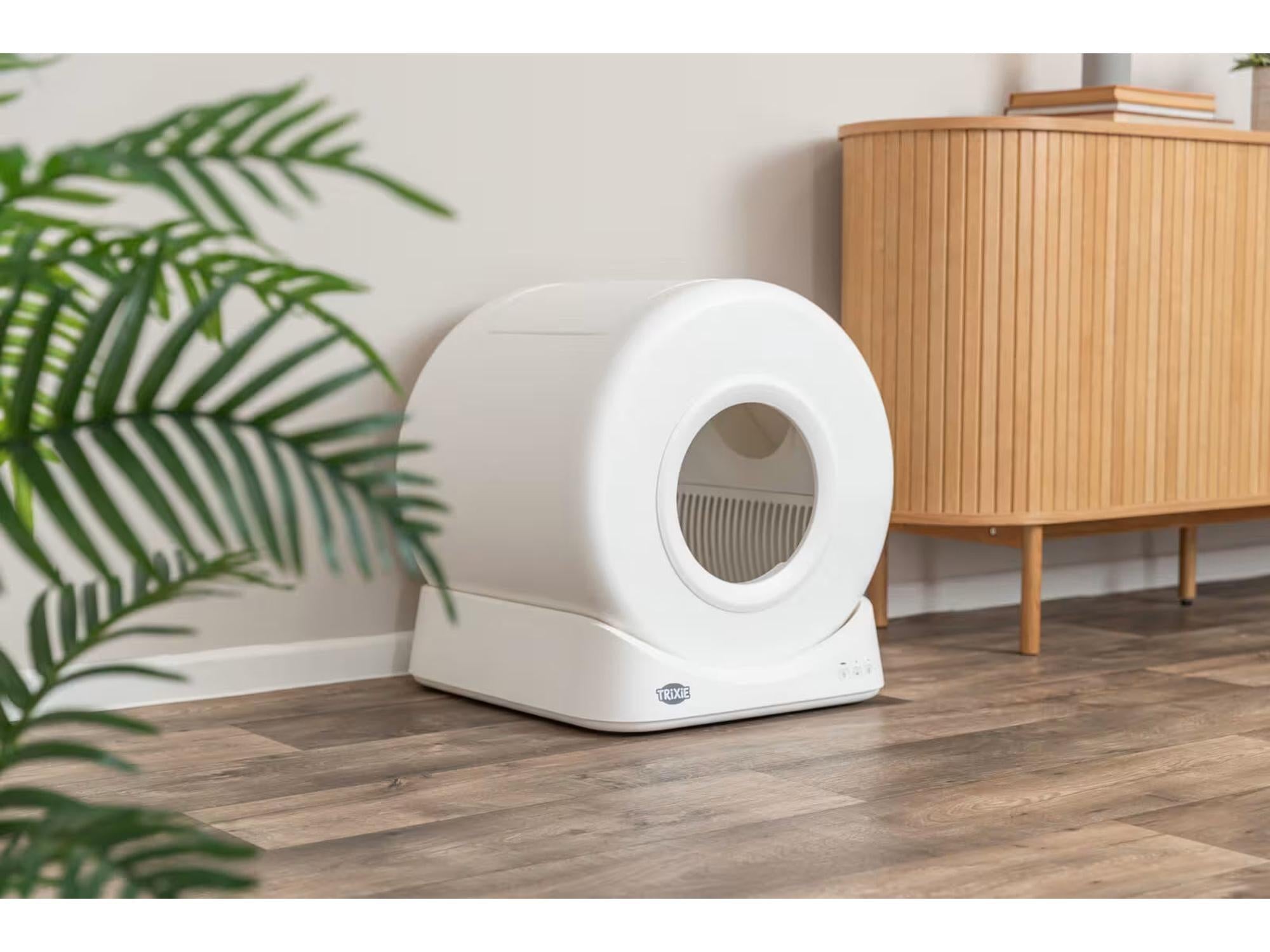 Hvit, rund TRIXIE Smart selvrensende kattedo i plast med åpen inngang, på tregulv.